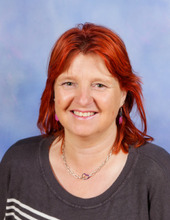A woman with bright red hair wearing a grey top smiles at the camera